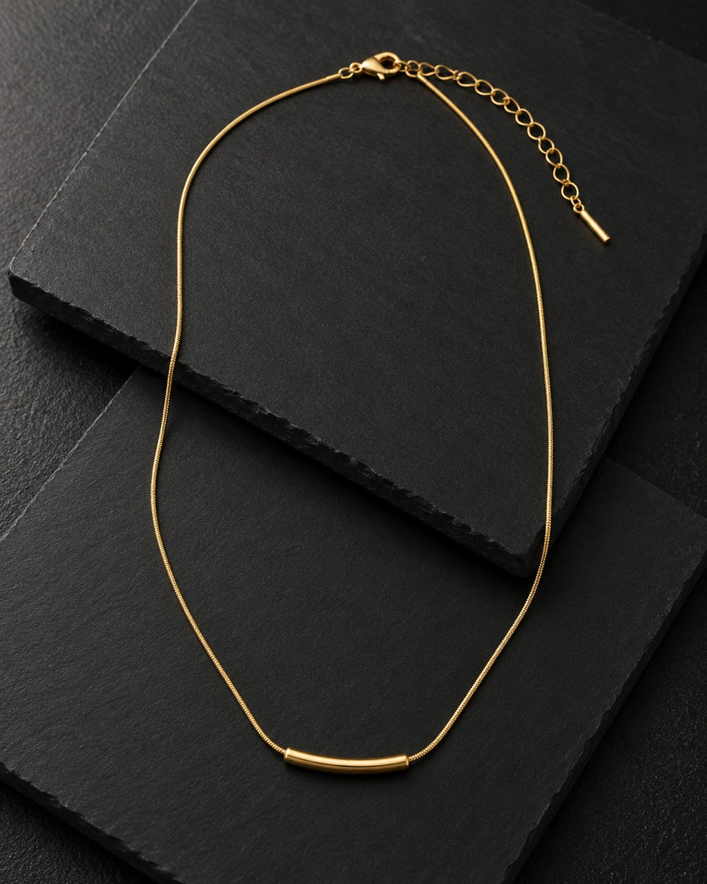 Minimal gold-tone bar necklace with a curved bar pendant on black slate