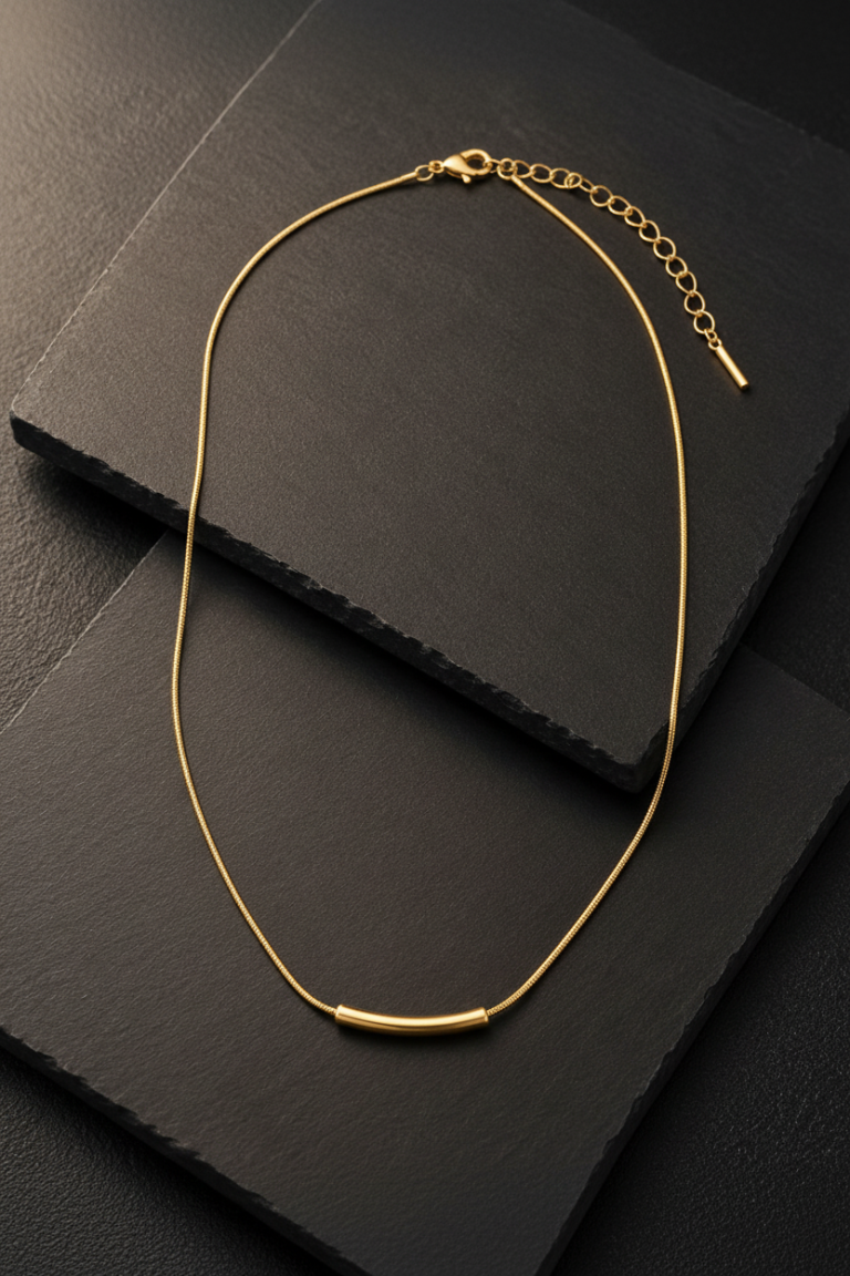 Minimal gold-tone bar necklace on a charcoal studio background